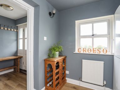 A small room with a wooden wine rack holding a plant near a window with letters spelling croeso on the sill at Bethania in Llangoed near Beaumaris