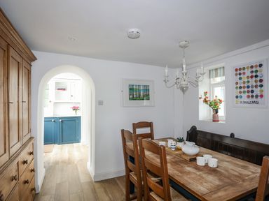 A dining room with wooden chairs and table with tea set hanging chandelier and arched doorway leading to a kitchen at Bethania in Llangoed near Beaumaris