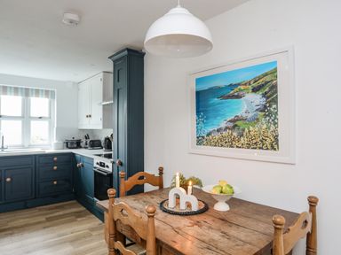 A kitchen with wooden dining table and chairs blue and white cabinets and a coastal painting on the wall at Bethania in Llangoed near Beaumaris