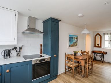 A kitchen with blue cabinets a wooden dining table with chairs and wall art at Bethania in Llangoed near Beaumaris