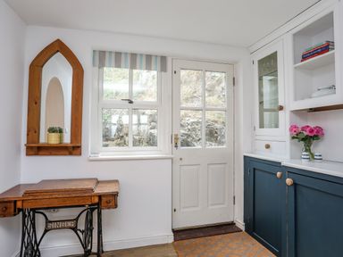 A room with a wooden antique sewing machine table a wooden framed mirror a window and a door with glass panes and blue and white cabinetry with pink flowers on the counter at Bethania in Llangoed near Beaumaris
