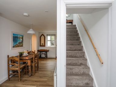 A dining area with wooden table and chairs next to a carpeted staircase with wooden handrail at Bethania Llangoed near Beaumaris