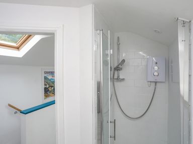 A bathroom shower area with a glass door a wall-mounted showerhead and electric water heater at Bethania in Llangoed near Beaumaris