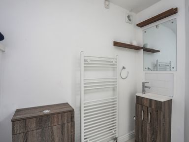 A bathroom with a small sink cabinet a mirror wooden shelves and a white towel radiator at Bethania in Llangoed near Beaumaris