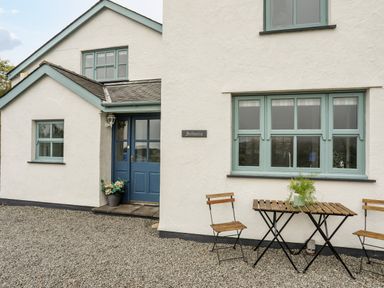 The exterior of a house with blue door and windows with wooden table and chairs on gravel at Bethania Llangoed near Beaumaris