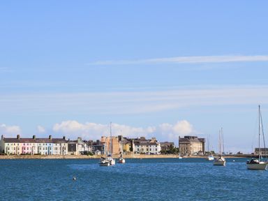 A waterfront view with several sailboats on the water and a row of buildings along the shore at Bethania in Llangoed near Beaumaris