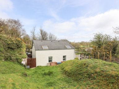 A white house with two skylights and windows surrounded by grassy hills and trees at Bethania in Llangoed near Beaumaris