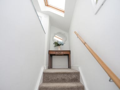A staircase with a carpet leading up to a wooden table with a vase of flowers and a decorative mirror at Bethania in Llangoed near Beaumaris