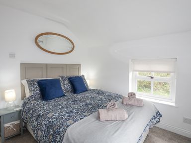 A bedroom with a patterned bedspread two rolled towels on the bed a window with a blind and a bedside table with a lamp at Bethania in Llangoed near Beaumaris