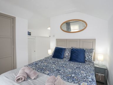 A bedroom with a bed with floral bedding and two blue pillows two bedside tables with lamps and towels on the bed at Bethania in Llangoed near Beaumaris