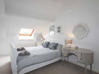 A bedroom with a white bed with pillows and folded towels a console table with a lamp and mirror and a small dresser under a skylight at Bethania in Llangoed near Beaumaris