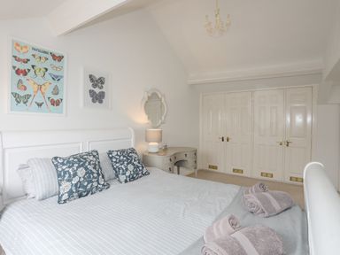 A bedroom with a bed with pillows and rolled towels a vanity table a lamp and butterfly pictures on the wall at Bethania in Llangoed near Beaumaris