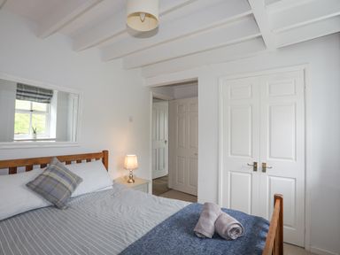 A bedroom with a wooden bed frame striped bedding a table lamp and a closet at Bethania in Llangoed near Beaumaris