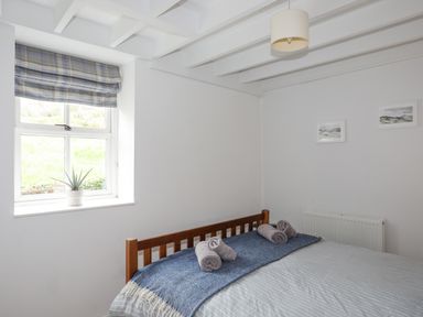 A bedroom with a wooden bed frame blue blanket and two rolled towels near a window with a plant on the sill at Bethania in Llangoed near Beaumaris