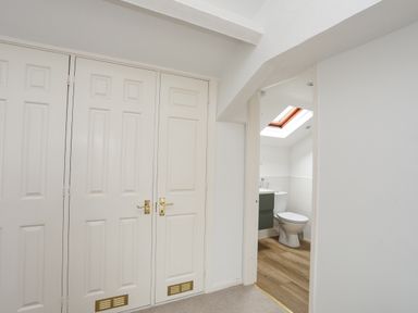 A hallway with white closet doors and a doorway leading to a bathroom with a toilet and skylight at Bethania in Llangoed near Beaumaris