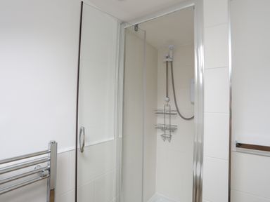 A shower area with glass door and metal shower caddy in a bathroom at Bethania in Llangoed near Beaumaris