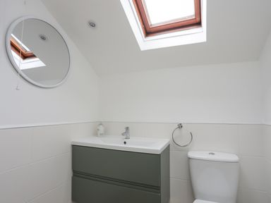 A bathroom with a wall-mounted sink cabinet a round mirror a toilet and a skylight window at Bethania in Llangoed near Beaumaris