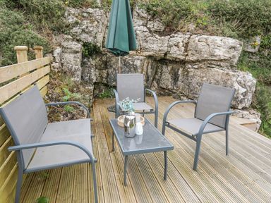 An outdoor seating area with chairs table and umbrella on a wooden deck surrounded by rocks and vegetation at Bethania in Llangoed near Beaumaris