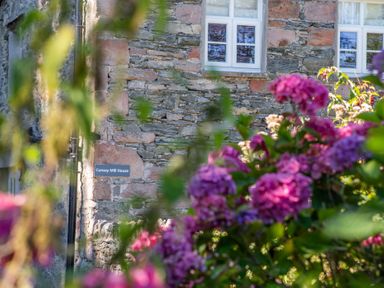 A stone wall house with white windows and pink flowers in the foreground at Cunsey Mill House Cunsey near Hawkshead