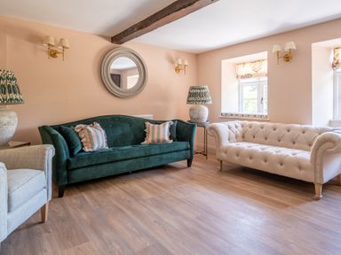 A living room with a green sofa, beige sofa, armchair, round wall mirror, lamps, and wooden floor at Cunsey Mill House Cunsey near Hawkshead
