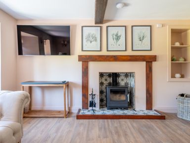 A living room with a wall-mounted television a wood-burning stove with patterned tile surround and wooden mantel at Cunsey Mill House Cunsey near Hawkshead