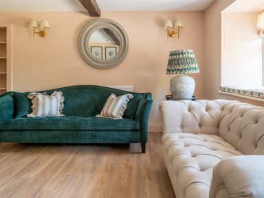 A living room with a green sofa with striped cushions a beige tufted sofa a round wall mirror and a lamp with patterned shade at Cunsey Mill House Cunsey near Hawkshead