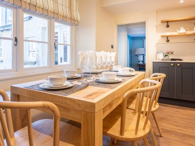 A dining area with a wooden table set with bowls plates and glasses next to window and kitchen cabinets at Cunsey Mill House in Cunsey near Hawkshead