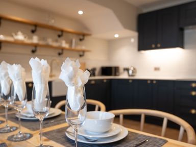 A dining table set with glasses and white napkins in a kitchen with dark cabinets and open shelves at Cunsey Mill House Cunsey near Hawkshead