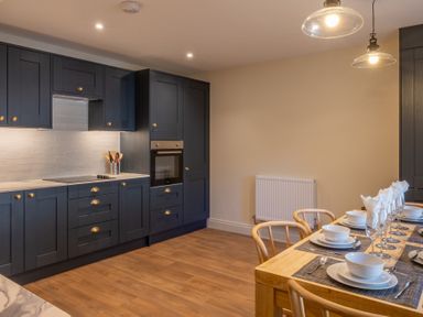 A kitchen with dark cabinets and a wooden dining table set with plates and glasses at Cunsey Mill House Cunsey near Hawkshead