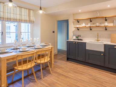 A kitchen and dining area with a set table and wooden chairs and dark cabinets at Cunsey Mill House Cunsey near Hawkshead