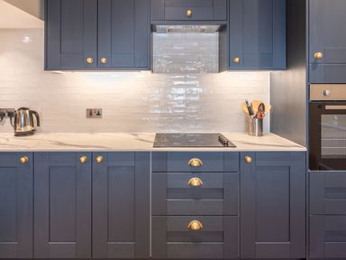A kitchen with dark cabinets a marble countertop an electric cooktop a kettle and cooking utensils at Cunsey Mill House Cunsey near Hawkshead
