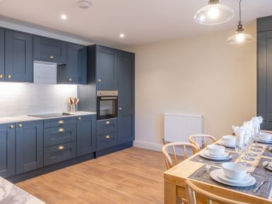 A kitchen with blue cabinets wooden floor and a dining table set with white dishes and glassware at Cunsey Mill House Cunsey near Hawkshead
