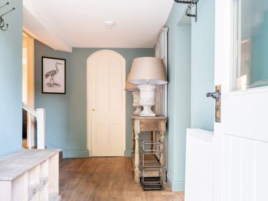 A hallway with wooden floor a cream door blue walls a wooden console table with two lamps and a metal rack at Cunsey Mill House Cunsey near Hawkshead