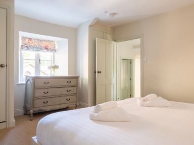 A bedroom with a bed, towels on the bed, a chest of drawers, a window with a floral curtain, and an open door at Cunsey Mill House Cunsey near Hawkshead