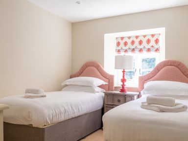 A bedroom with two single beds with pink headboards and a wooden nightstand with a red lamp at Cunsey Mill House Cunsey near Hawkshead