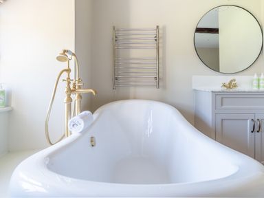 A bathroom with a white freestanding bathtub gold faucet round mirror and grey vanity at Cunsey Mill House in Cunsey near Hawkshead