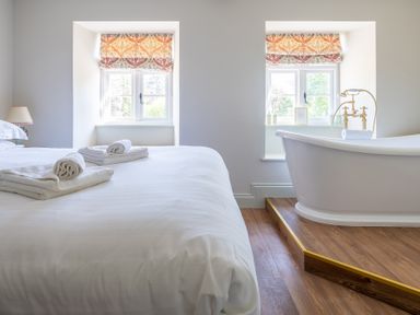 A bedroom with a double bed next to a freestanding bathtub on a wooden platform at Cunsey Mill House Cunsey near Hawkshead