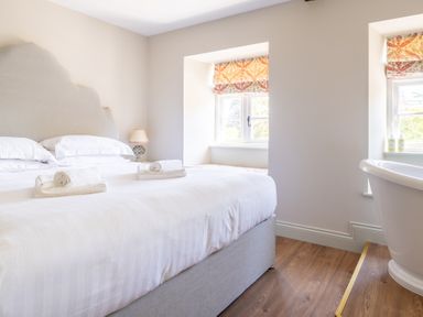 A bedroom with a large bed with white linens a bedside lamp two windows and a freestanding bathtub at Cunsey Mill House Cunsey near Hawkshead