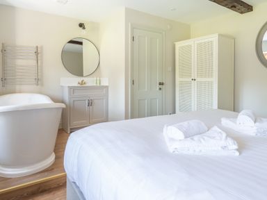A bedroom with a bed holding folded towels a bathtub a vanity with a round mirror a wall-mounted towel rack a door and a wardrobe at Cunsey Mill House Cunsey near Hawkshead