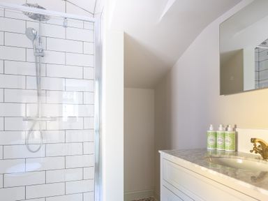 A bathroom with a glass shower enclosure and a white tiled wall next to a sink with marble countertop and three bottles at Cunsey Mill House Cunsey near Hawkshead