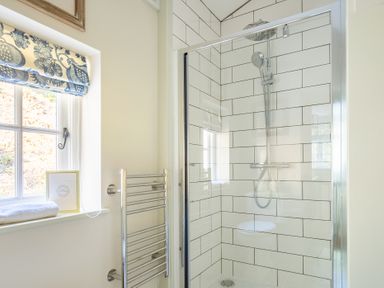 A bathroom with a glass shower enclosure a chrome shower fixture a heated towel rail and a window with a blue patterned Roman blind at Cunsey Mill House Cunsey near Hawkshead