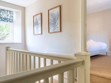A hallway with white railings paintings on the wall and a window with a patterned blind next to a bedroom with a bed at Cunsey Mill House Cunsey near Hawkshead