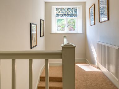 A stair landing with framed pictures on walls a window with floral blinds and a radiator at Cunsey Mill House Cunsey near Hawkshead