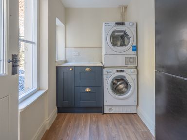 A laundry room with a stacked washer and dryer next to blue cabinets with gold handles at Cunsey Mill House Cunsey near Hawkshead