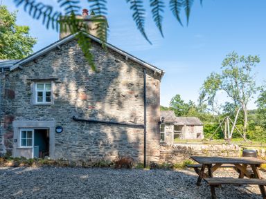 Stone house exterior with gravel ground and wooden picnic table at Cunsey Mill House Cunsey near Hawkshead