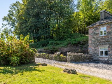 A stone building with white windows next to a gravel path and grassy area with trees in the background at Cunsey Mill House Cunsey near Hawkshead