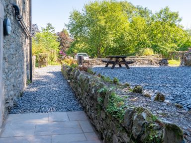 An outdoor area with stone walls trees a wooden picnic table a stone pathway and a parked car at Cunsey Mill House Cunsey near Hawkshead