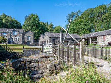 A stone house and outbuildings with wooden fences and greenery at Cunsey Mill House Cunsey near Hawkshead