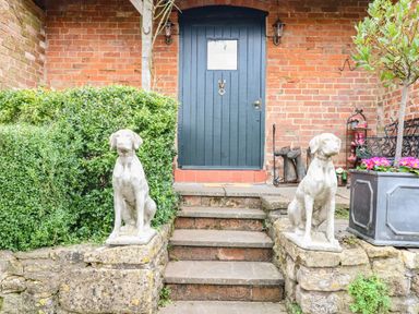 A front entrance with stone dog statues on either side of stairs leading to a dark wooden door at The Cheese Room in Stretton-On-Fosse