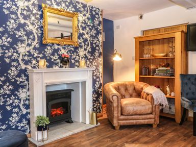 A lounge area with a leather chair a white fireplace and wooden bookshelf at The Cheese Room in Stretton-On-Fosse